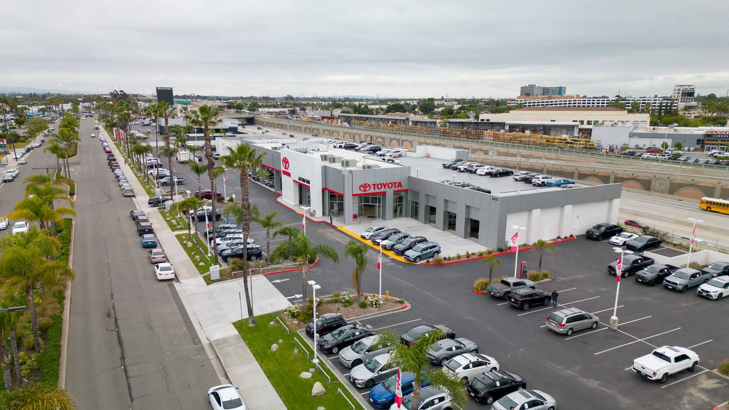 Exterior view of AutoNation Toyota Buena Park shot from a drone. Cloudy day, cars parked on the street with palm trees.
