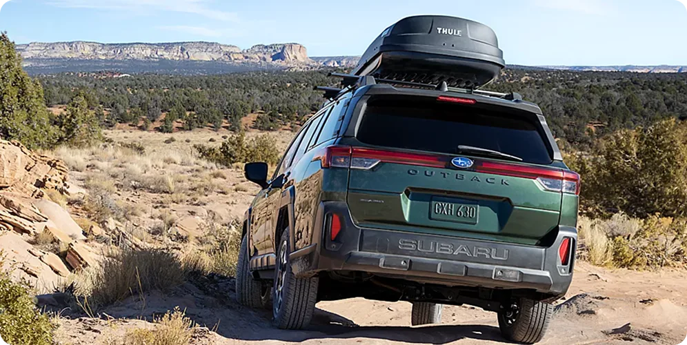 A Subaru Outback with a roof cargo box climbing over rock ledges