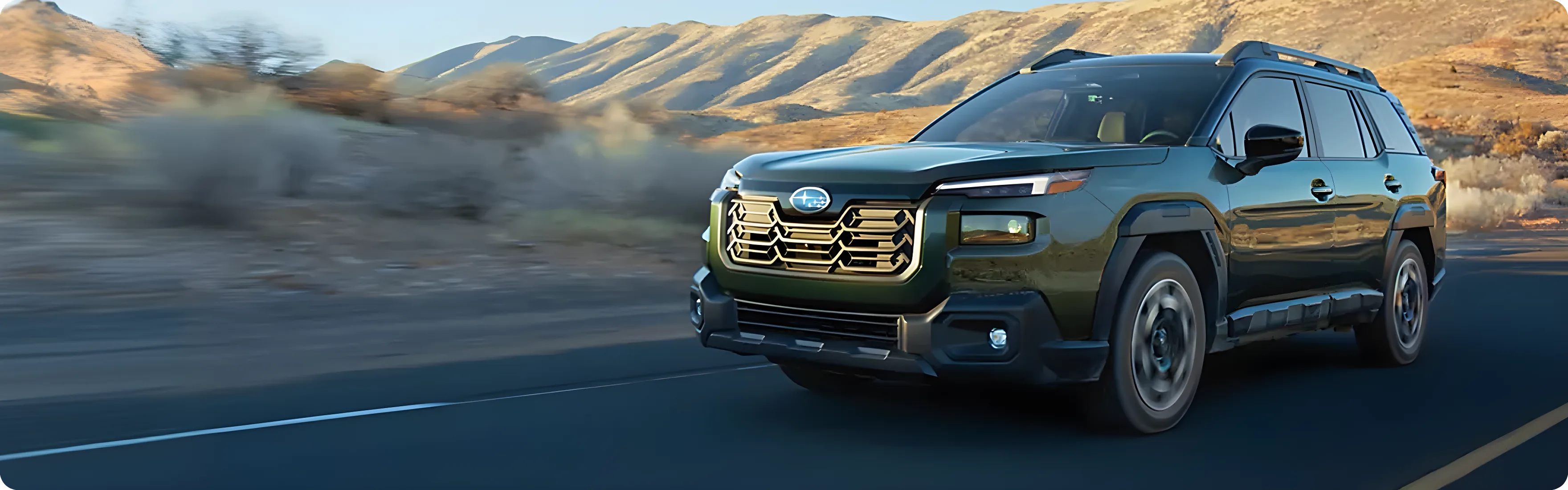 A green Subaru Outback driving a long open road through dry hills