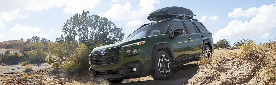 A green Outback Wilderness with a roof box parked on rock ledges