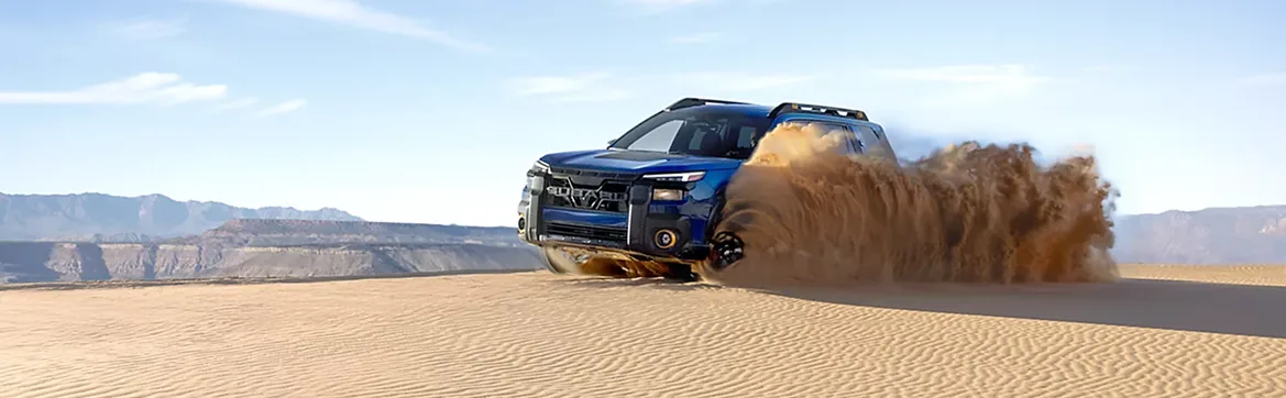 A blue Subaru Outback driving across open sand dunes