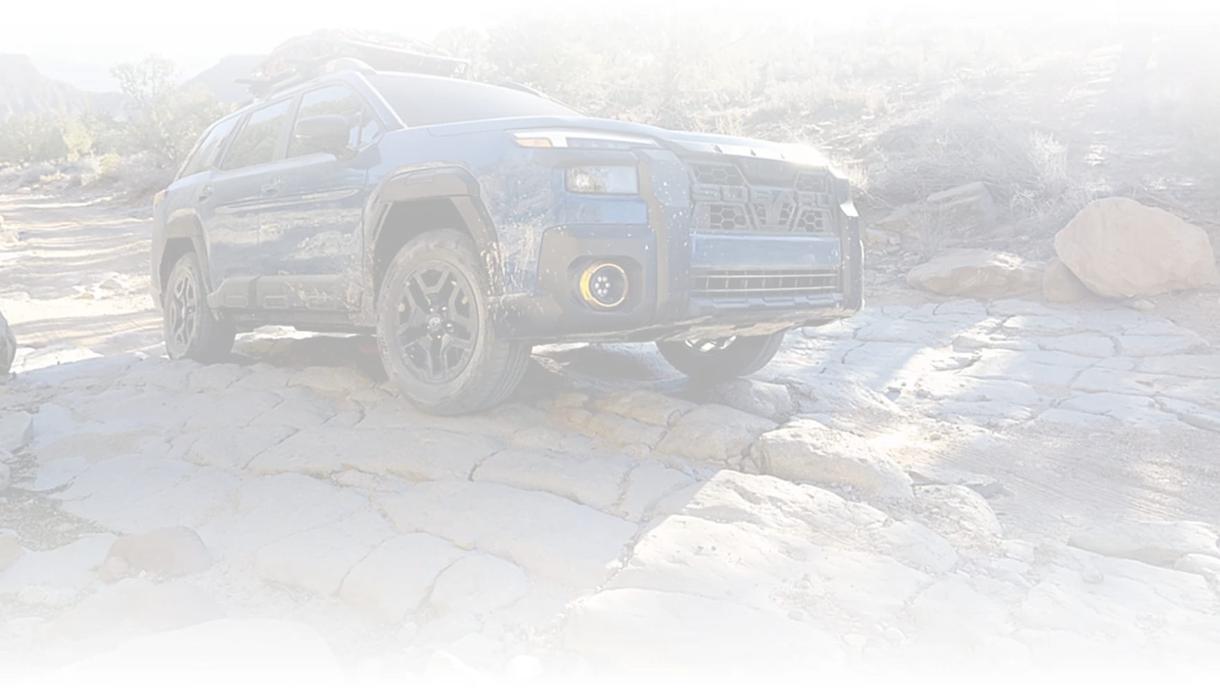 A blue Subaru Outback crossing a rocky stream bed