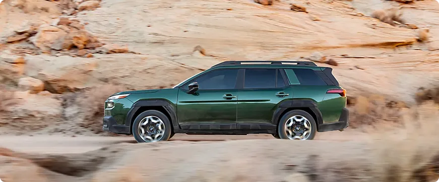 A green Subaru Outback Wilderness driving across red rock