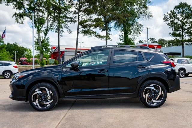 A black Subaru Crosstrek shown in profile on the Baldwin Subaru lot beneath tall pines and a blue sky