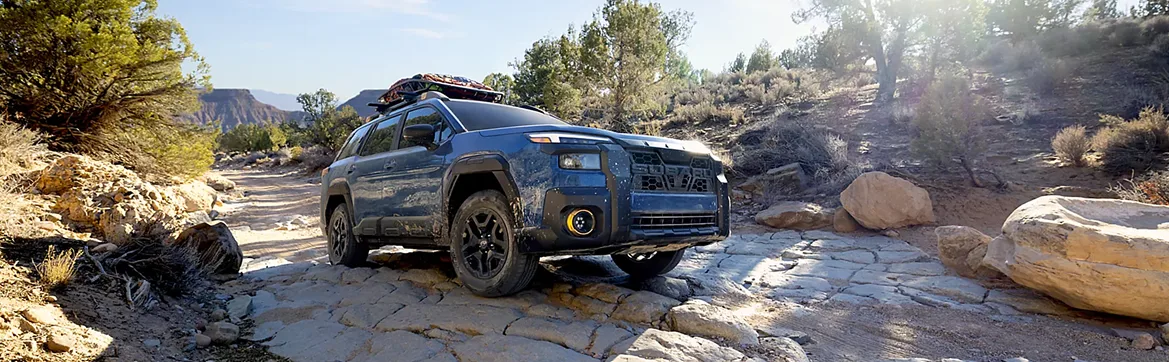 A blue Subaru Outback crossing a rocky stream bed