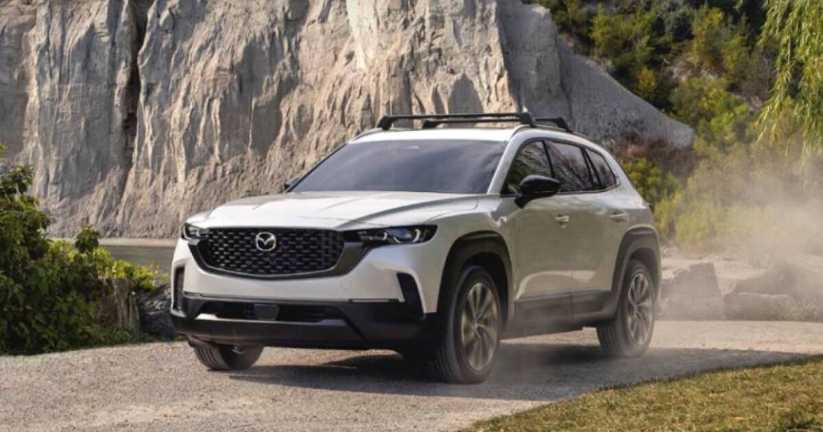 2026 Mazda CX-50 Hybrid A 2026 Mazda CX-50 Hybrid driving on a gravel road near rocky terrain.