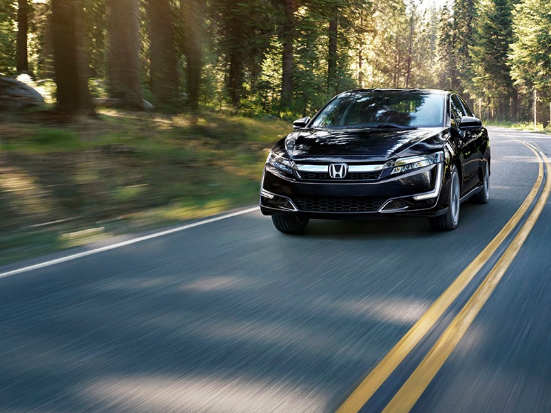 Honda Clarity Plug-in Hybrid a black Honda Clarity Plug-in Hybrid driving on a road in a forest.