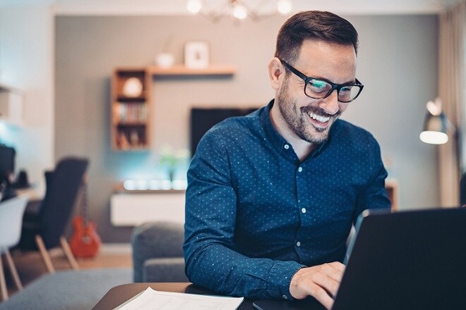 Man smiling while sitting at the table looking at a laptop