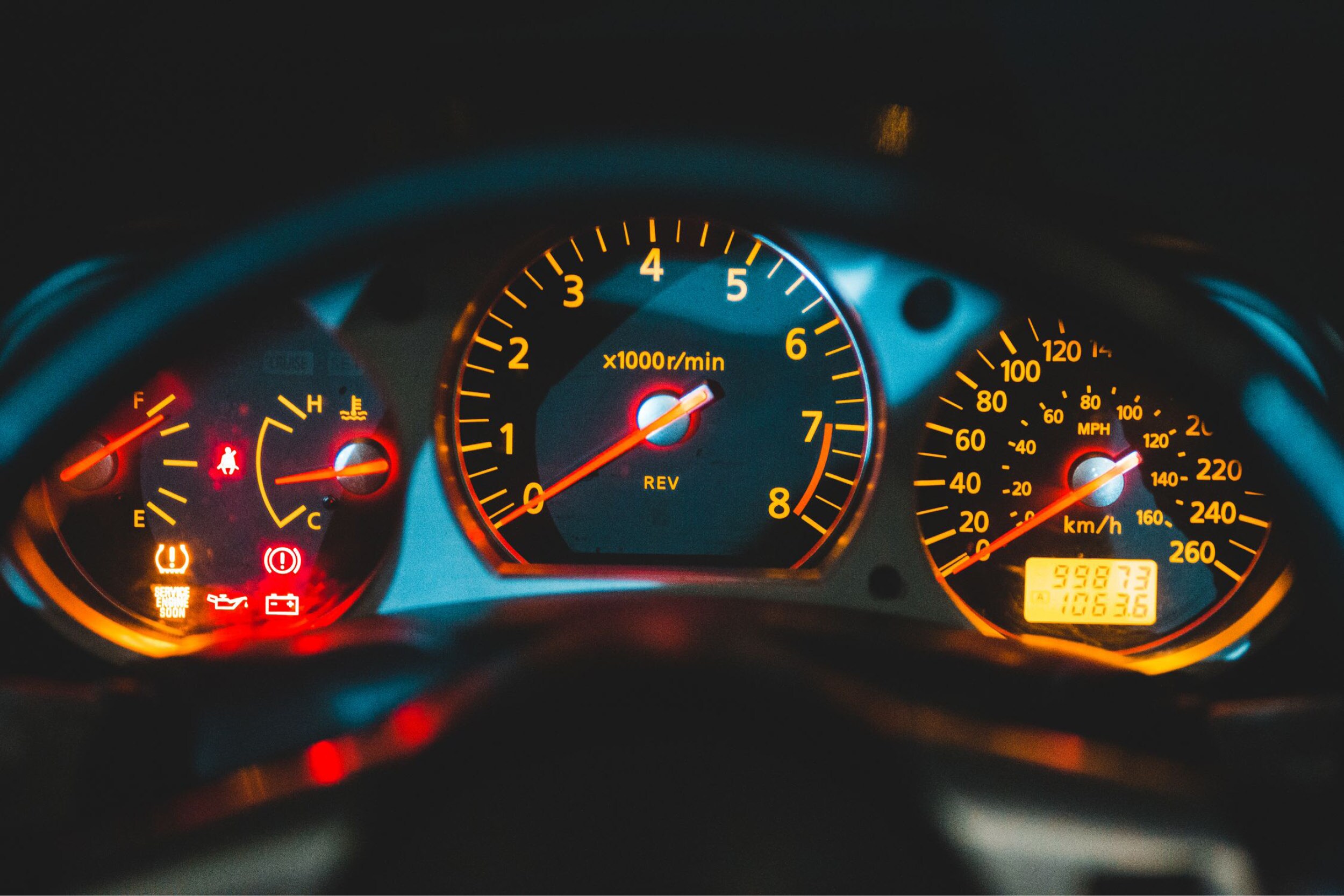 A close-up of a vehicle dashboard showing the red battery warning light and the check engine light illuminated.