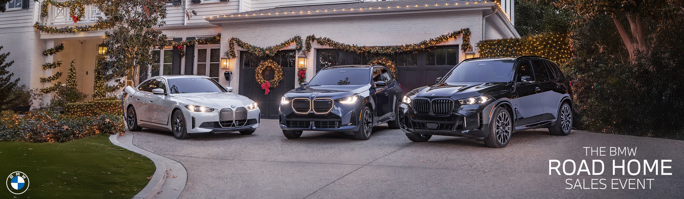 BMW Road Home Sales Event banner featuring a BMW model lineup on display and winter holiday decorations