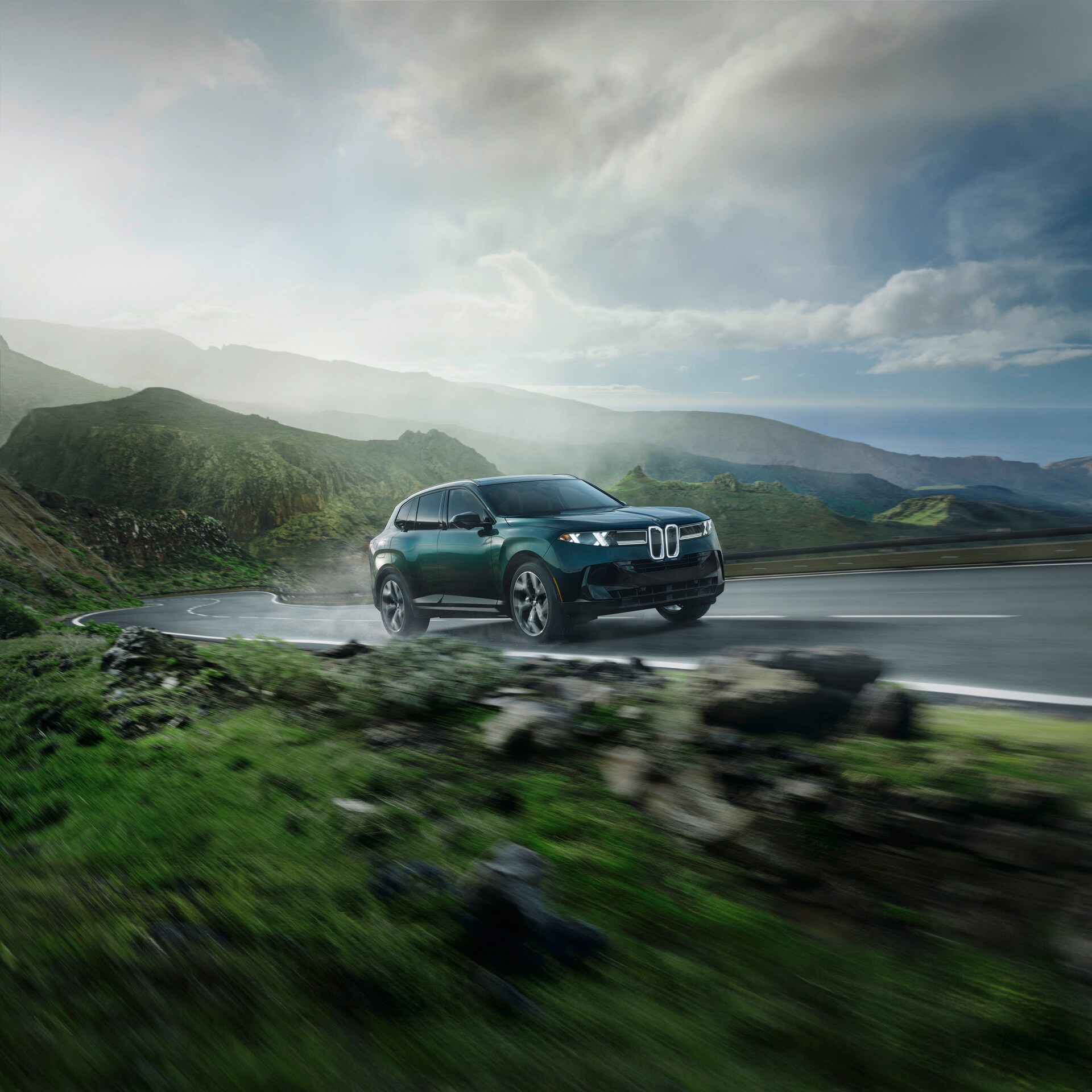 Green BMW X5 traveling along a winding mountain road, showing its new front lighting