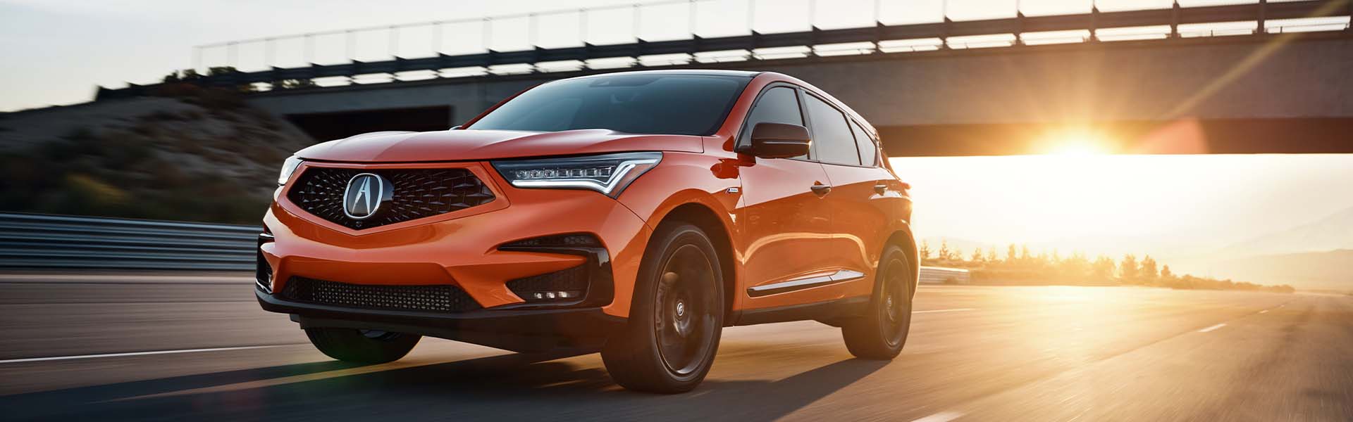 Compare the 2021 Acura RDX vs. the 2022 Audi Q5 at Bobby Rahal Acura | Orange 2021 Acura RDX Driving on Highway at Sunset