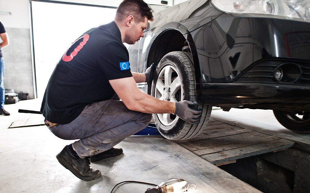 Learn Maintenance Warning Signs at Bobby Rahal Acura in Mechanicsburg, PA | Man wearing black shirt and black gloves is inspecting vehicle tires while vehicle is lifted up