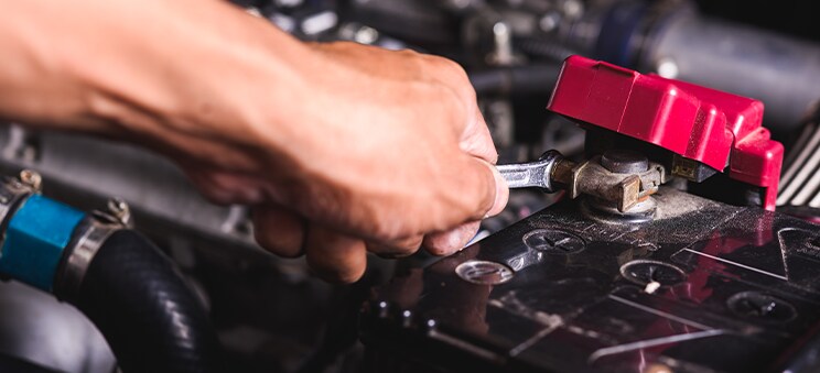 Everything You Need to Know about Your Car Battery at Bobby Rahal Acura | A person's hand tighting up a loose battery connecter by using a hand wrench