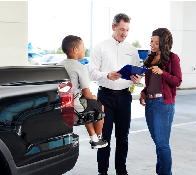 Bobby Rahal Honda is a Car Dealership near Lewisberry PA | Customer Talking to Sales Advisor While Child Sits on Tailgate of Honda Ridgeline Inside Dealership Showroom
