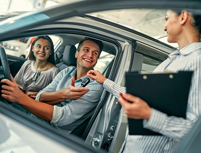 Trade in my leased car at Bobby Rahal Lexus of Lancaster County in Ephrata, PA | Couple sitting in new car while smiling and being handed the car keys to test drive
