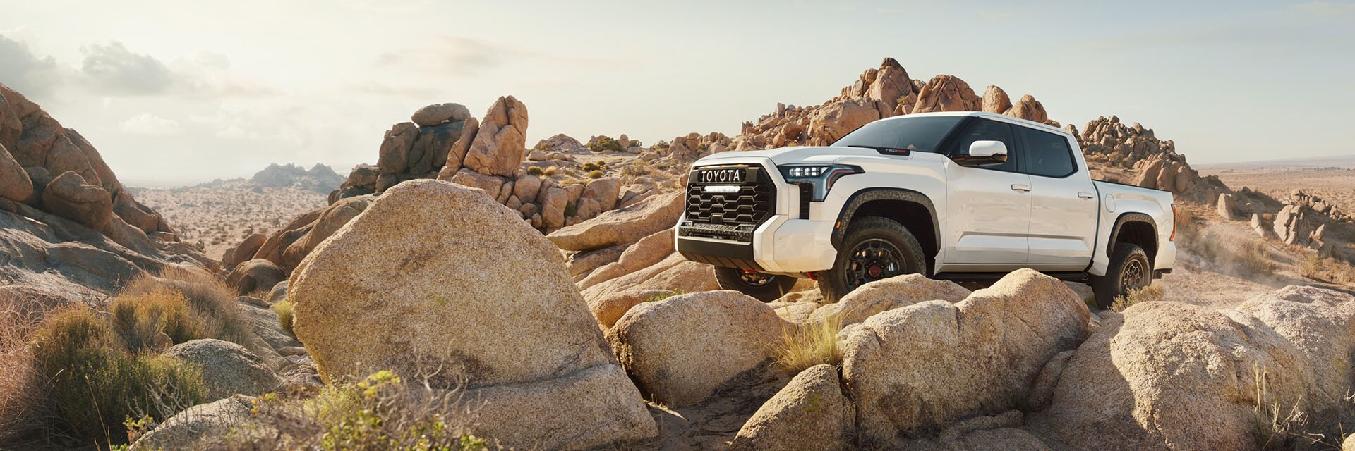 Leasing versus Buying a Toyota at Bobby Rahal Toyota in Mechanicsburg, PA | White 2022 Toyota Tundra Driving on Rocks in Mountains Facing Left