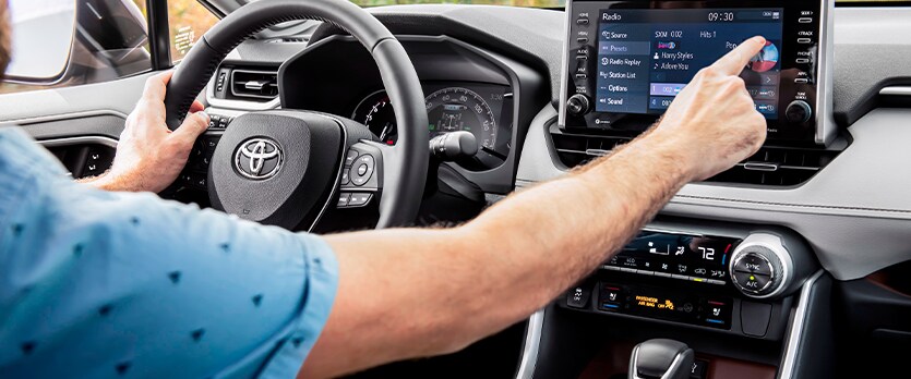 Everything You Need to Know about Your Car Battery at Bobby Rahal Toyota | Interior of a Toyota where a man is touching the infotainment system with his right hand