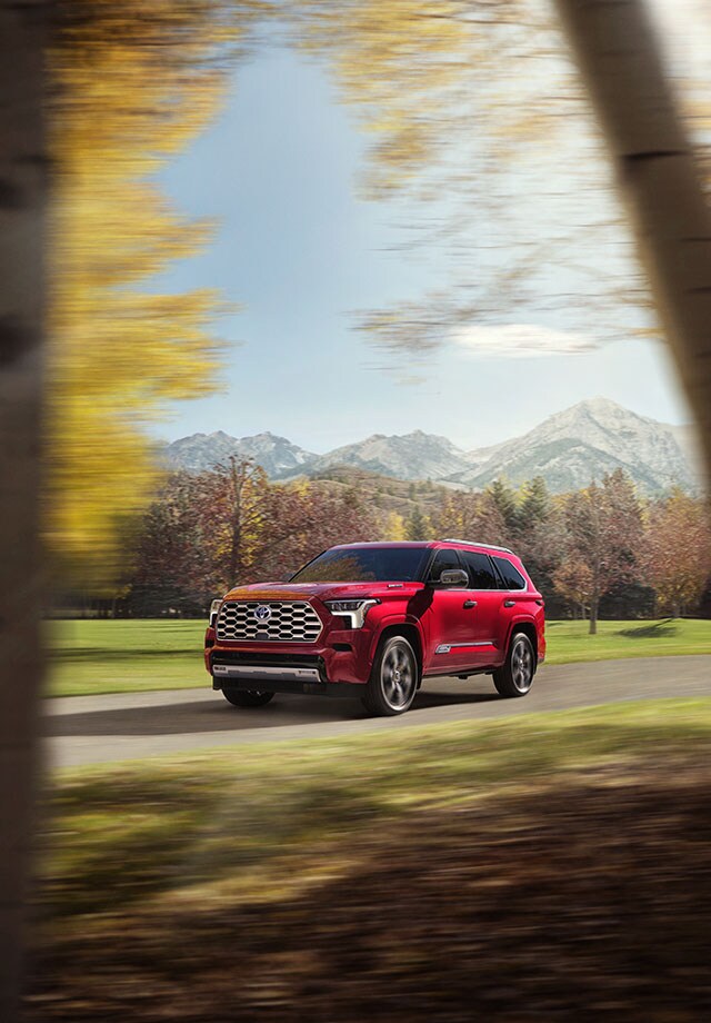 Model Features of the All-New 2023 Toyota Sequoia at Bobby Rahal Toyota | Red 2023 Toyota Sequoia Driving through Woodlands Facing Left