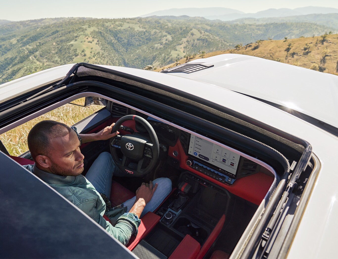 2023 Toyota Tundra vs. 2023 Ford F-150 at Bobby Rahal Toyota | Aerial view from the top of a White Toyota Tundra sunroof showing the red interior while a man is driving