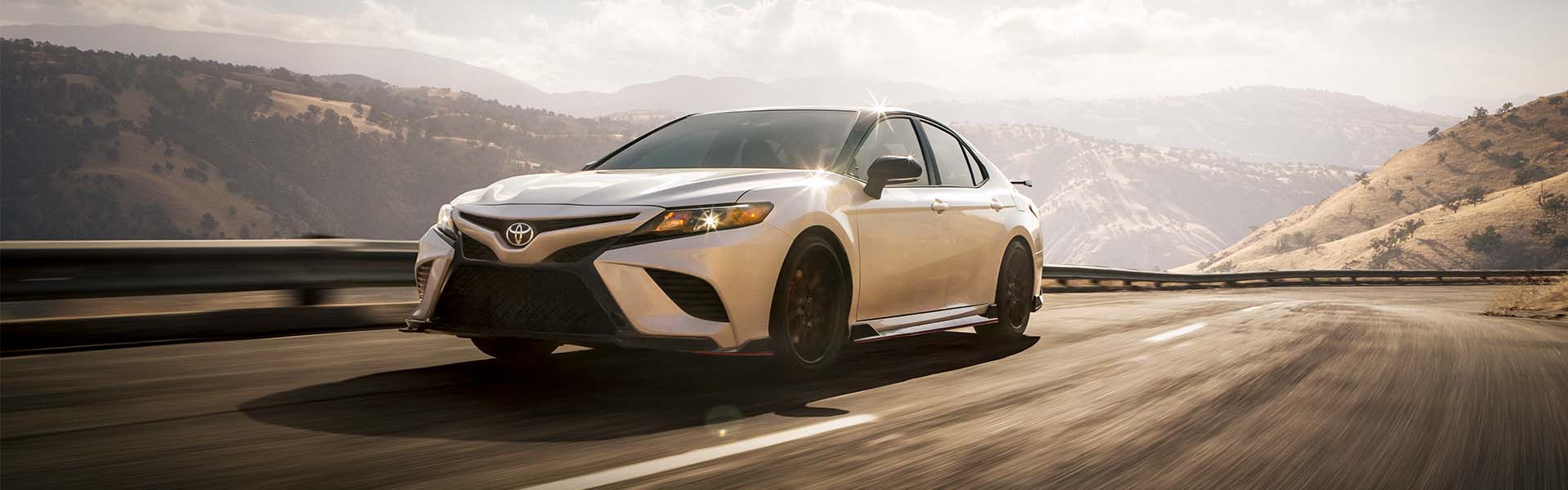 Model Features of the 2022 Toyota Camry at Bobby Rahal Toyota | White 2022 Toyota Camry Driving on Road with Mountains in the Distance at Sunset