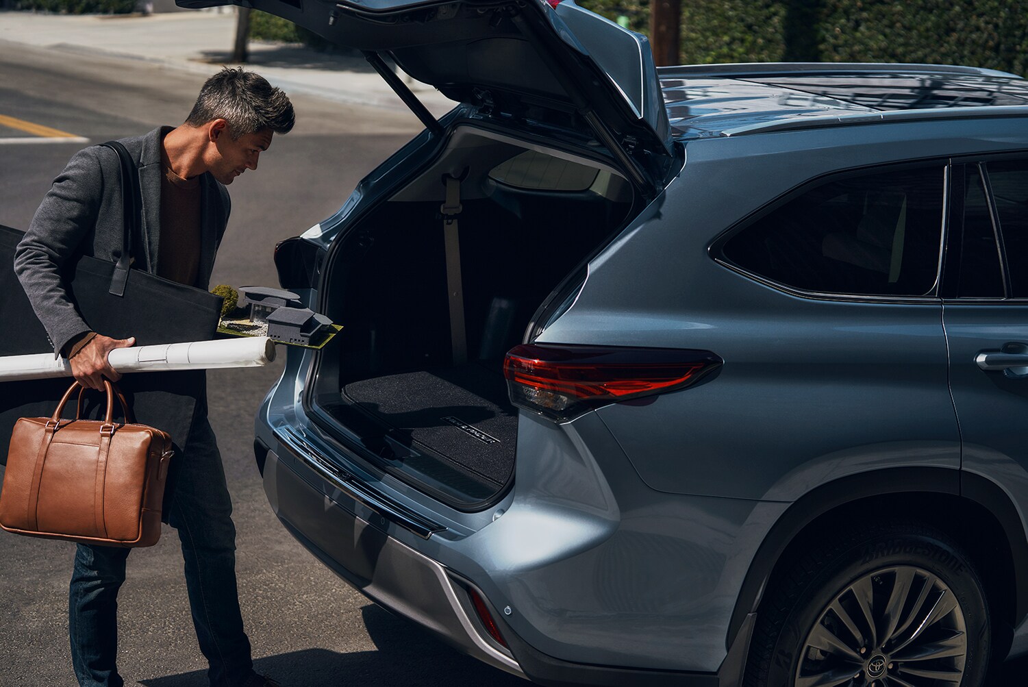 Compare the 2021 Toyota Highlander vs. the 2021 Subaru Ascent at Bobby Rahal Toyota | Business man putting work supplies in 2021 Toyota Highlander trunk