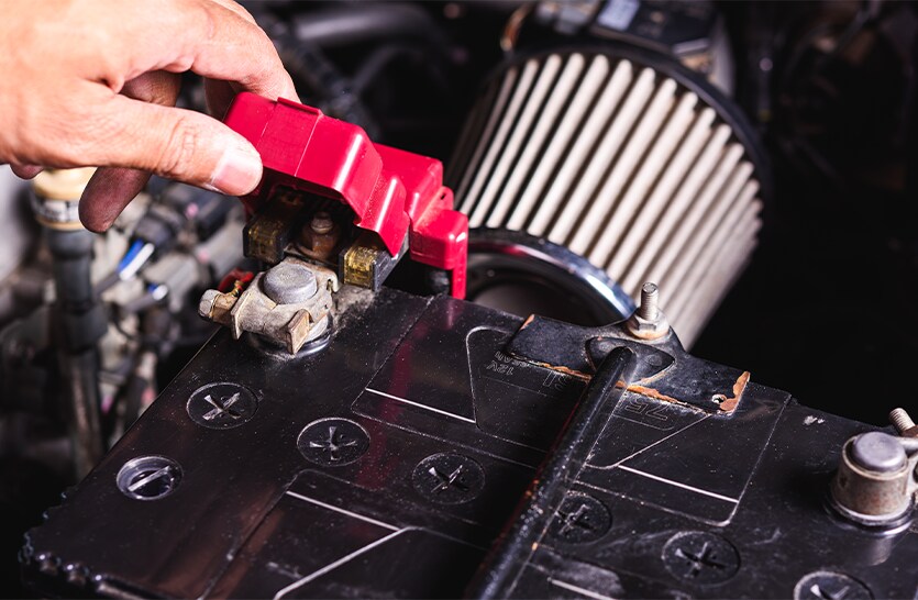 Everything You Need to Know about Your Car Battery at Bobby Rahal Toyota | Man lifting red battery cover to inspect battery terminal