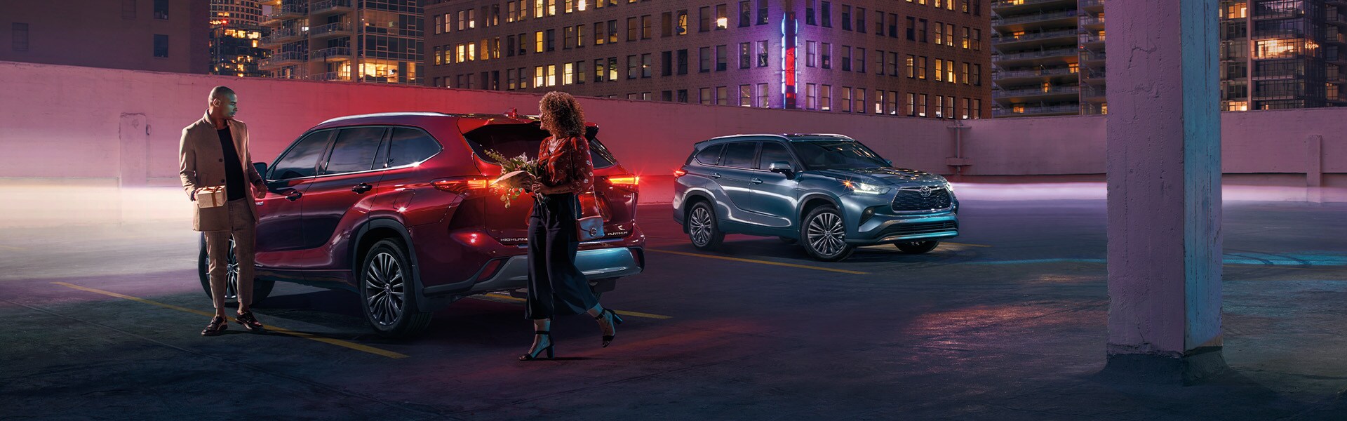 Model Features of the 2022 Toyota Highlander Hybrid at Bobby Rahal Toyota | Red and Blue Highlander Hybrid Vehicles Parked Next to Each Other in Parking Garage in City at Night