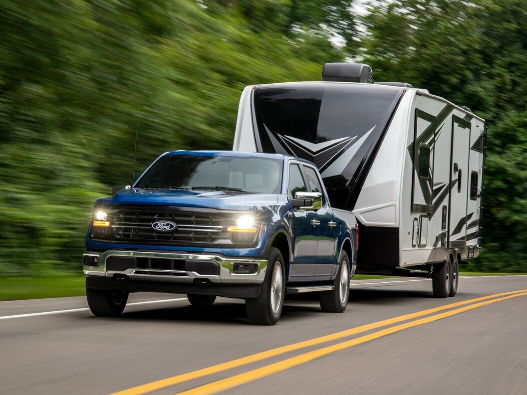Blue Ford F-150 Hybrid towing a camper trailer on a scenic road