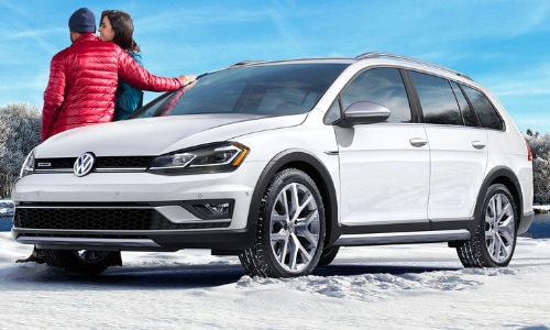 2020 Volkswagen Golf Alltrack white parked in a snowy mound couple leaning on hood