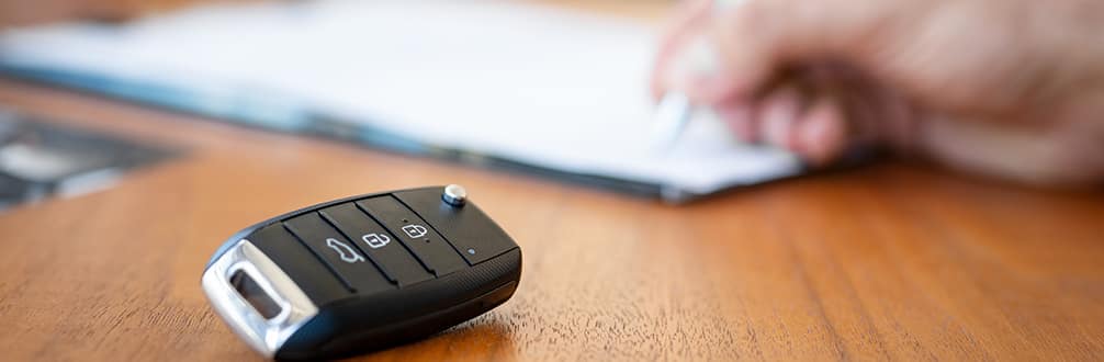 Boch Nissan South is a Family Owned Dealership near Foxborough, MA | Closeup of customer signing financial documents with key fob in foreground