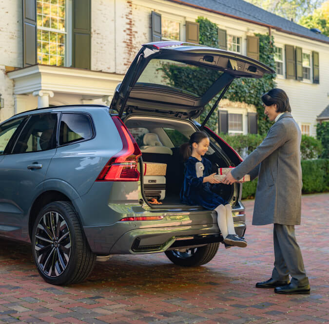 Exterior shot of Volvo XC60 with open tailgate, a man and a child load luggage into the trunk.