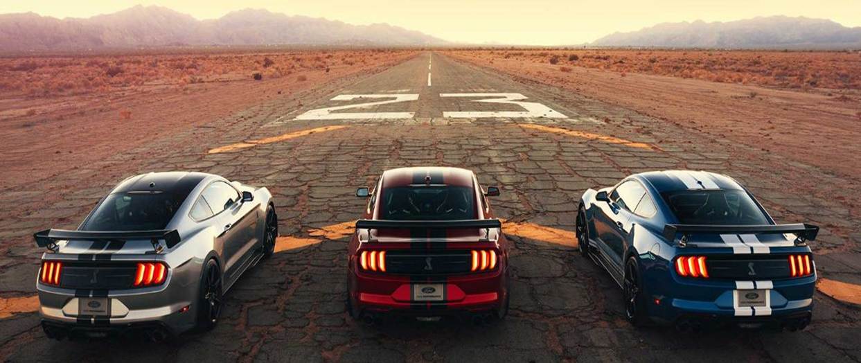 2020-ford-shelby-mustang-gt500-performance-bowen-scarff-ford-dealership-seattle.jpg Back view of three 2020 Ford Shelby Mustang GT500s, one silver, red, and blue on a dusty, cracked desert road with a worn, white number 23 in front. Mountains in the distance frame a straight, never-ending road.