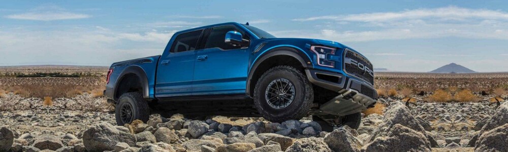Price of the 2019 Ford F-150 Raptor at Bowen Scarff Ford in Kent WA near Seattle.png Passenger side view of a velocity blue 2019 Ford F-150 Raptor truck easily driving over big rocks under a clear blue sky