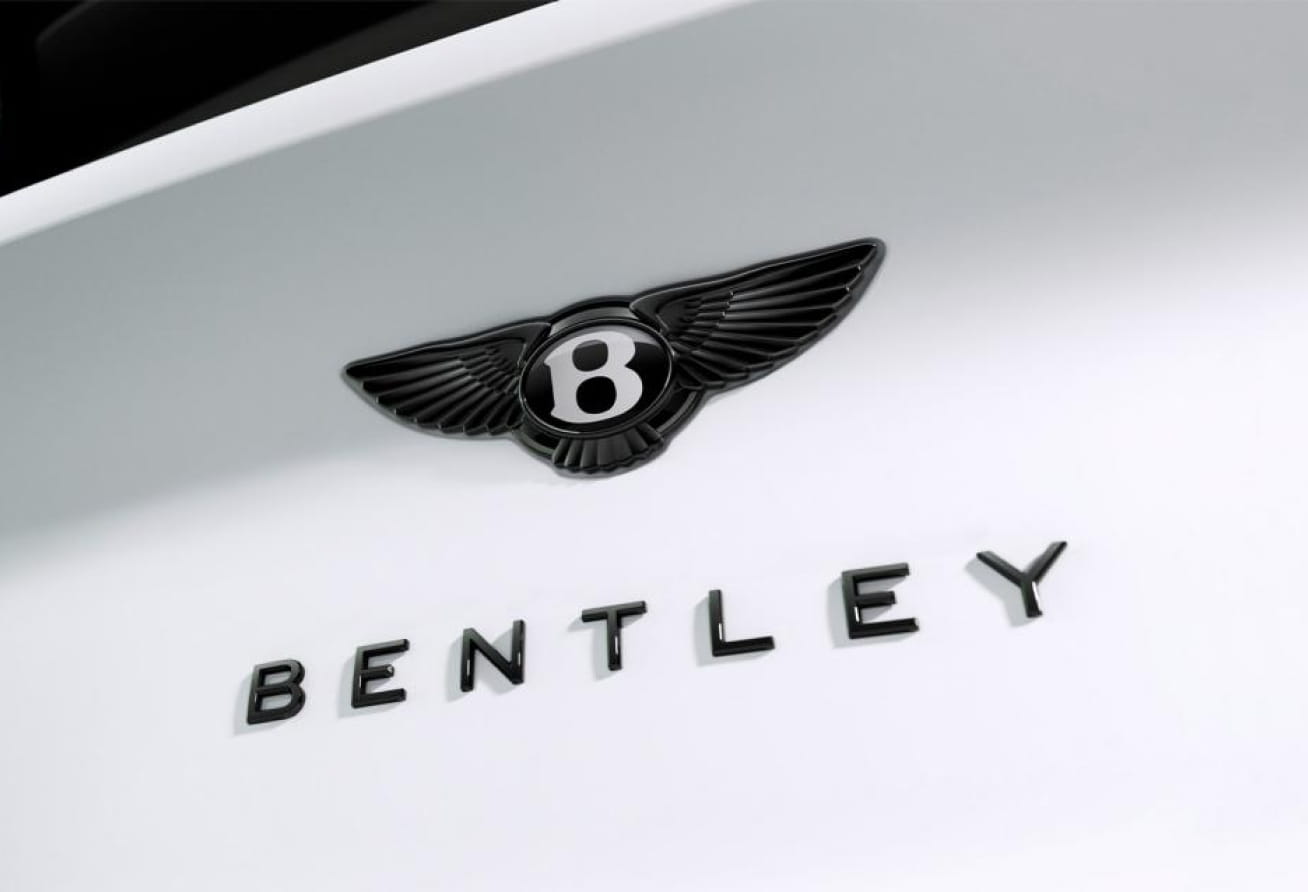 Close-up of the Bentley winged emblem and lettering on a white vehicle.