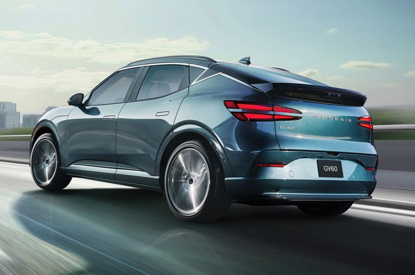 2026 Genesis GV60 SUV driving on a highway and showcasing its futuristic design and sharp lines under a clear sky with a modern cityscape in the background.