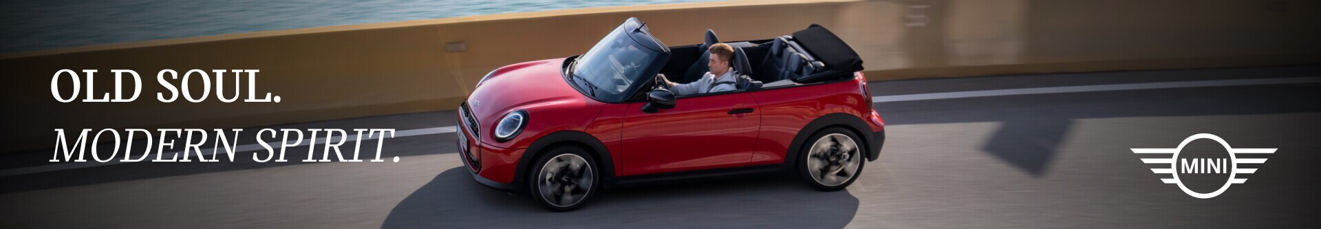 MINI Cooper Convertible drives with its top down along a coastal highway.