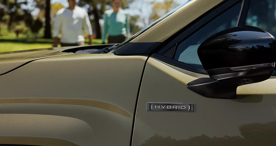 Close-up of the 2026 Subaru Forester Hybrid front fender and HYBRID badge, with two people walking in the background