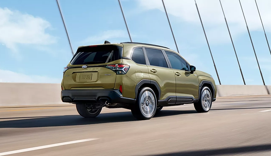 Green 2026 Subaru Forester Hybrid driving across a bridge, rear three-quarter view