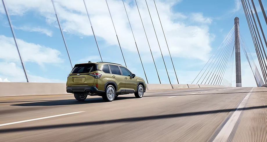 Green 2026 Subaru Forester Hybrid driving across a cable-stayed bridge, rear three-quarter view