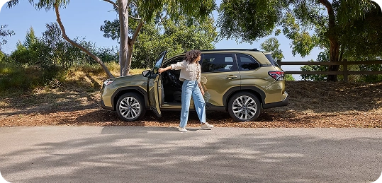 Green 2026 Subaru Forester Hybrid parked at the roadside as a woman opens the driver's door
