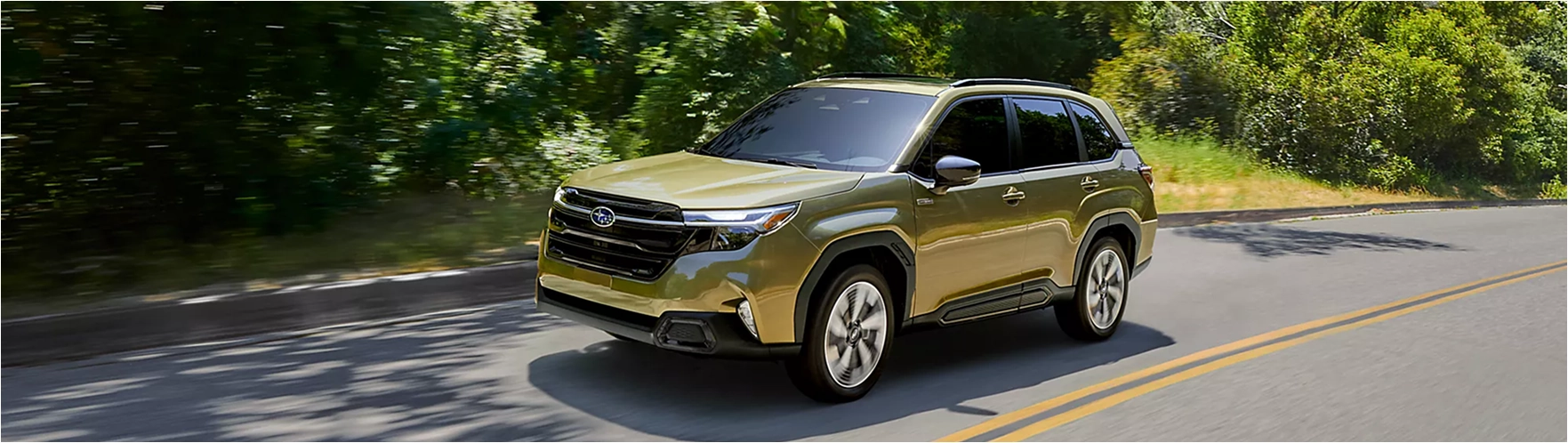 Green 2026 Subaru Forester Hybrid driving on a tree-lined road, front three-quarter view