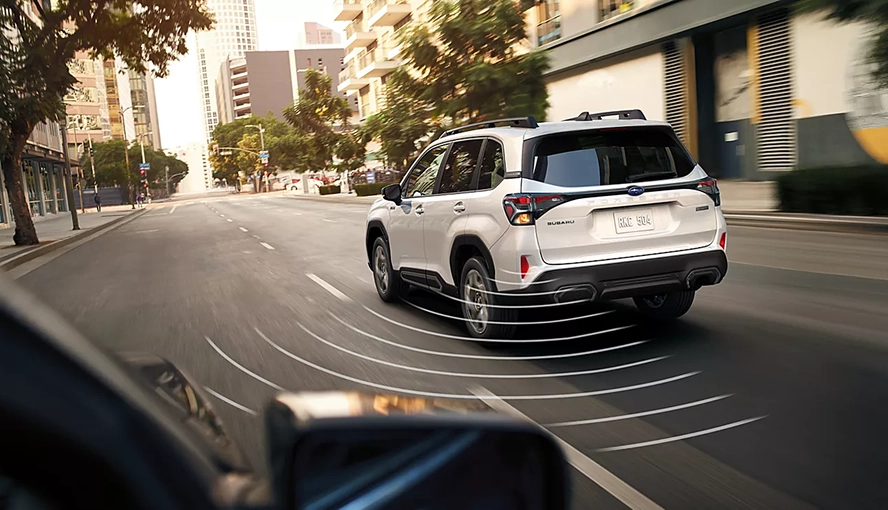White 2026 Subaru Forester Hybrid driving on a city street, rear three-quarter view, with rear detection sensors visualized
