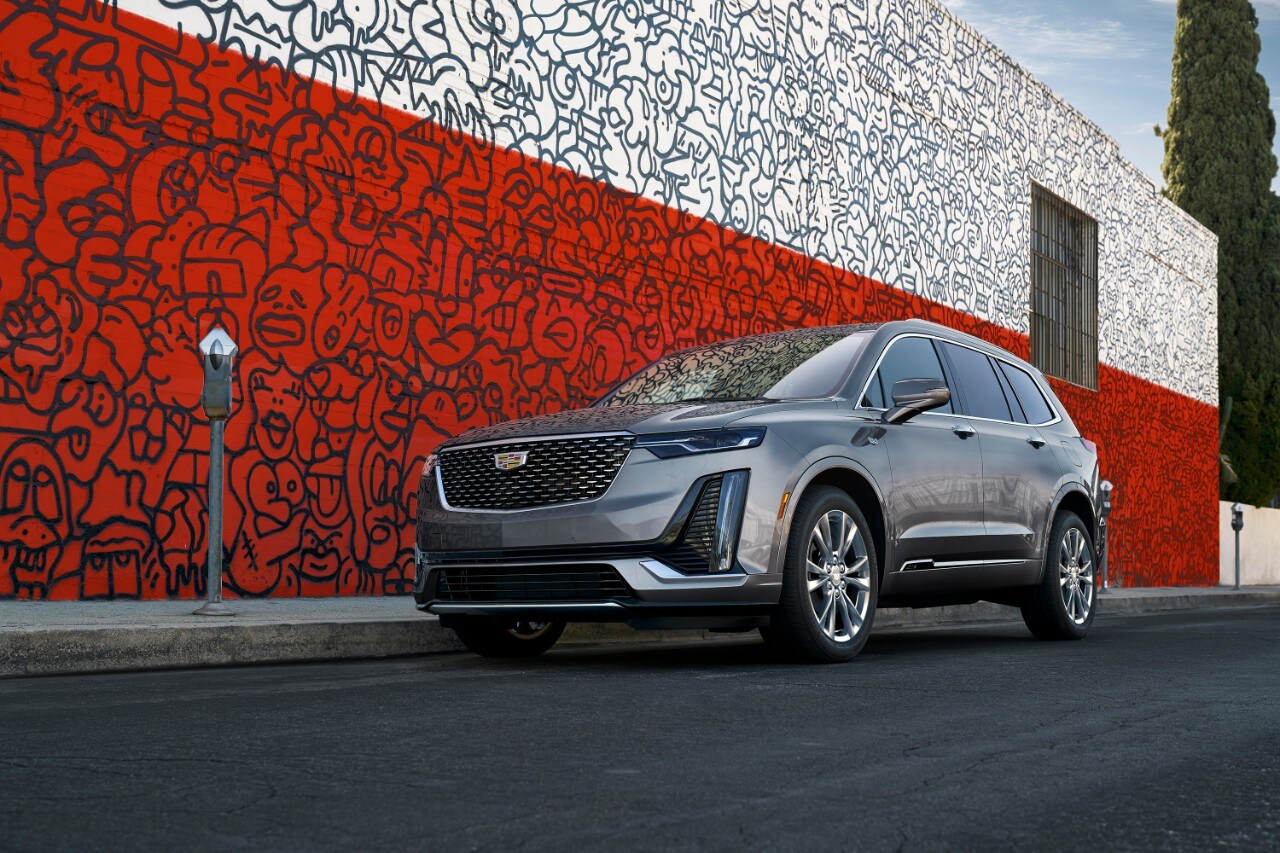 cadillac-xt6-luxury-2021-cadillac-laval-01.jpg Cadillac XT6 Luxury 2021 couleur gris, stationné sur le long d'un mur rouge et blanc avec graffitis
