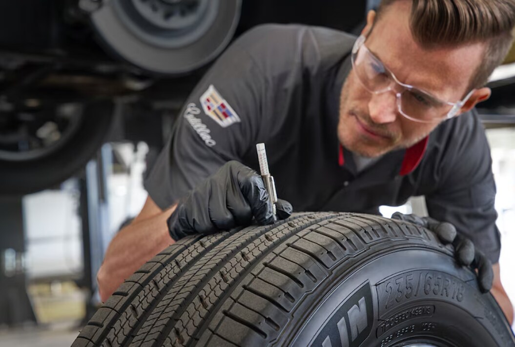 A certified Cadillac technician wearing goggles measures the tread depth on a tire A certified Cadillac technician wearing goggles measures the tread depth on a tire