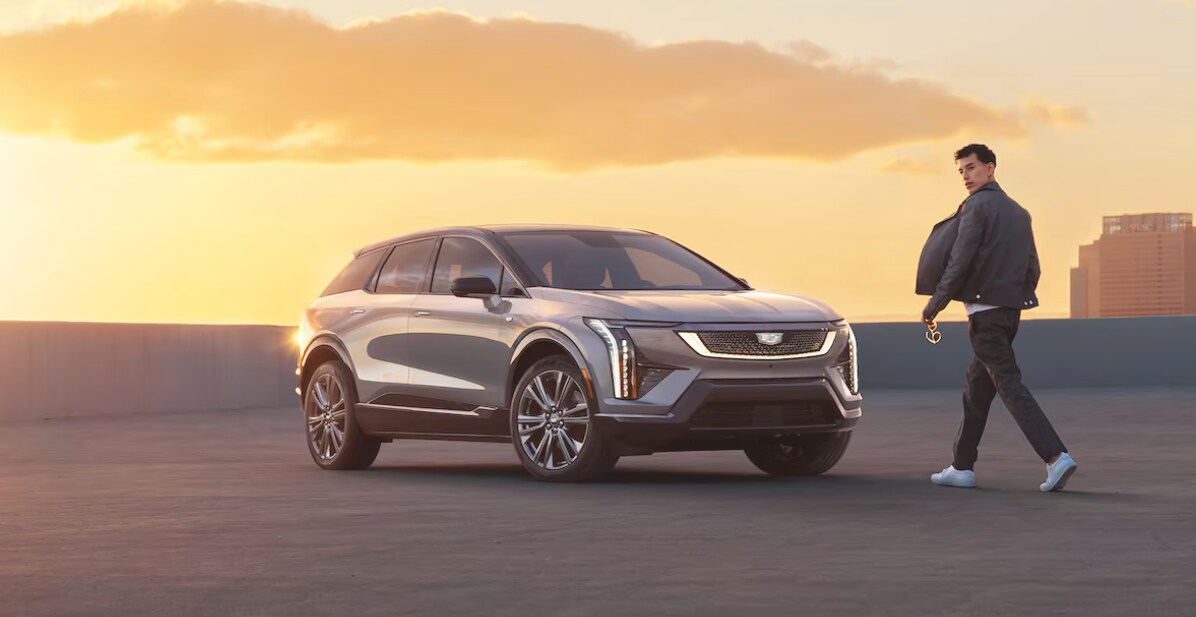 A young man walks towards a 2025 Cadillac OPTIQ parked on a rooftop at sunset A young man walks towards a 2025 Cadillac OPTIQ parked on a rooftop at sunset