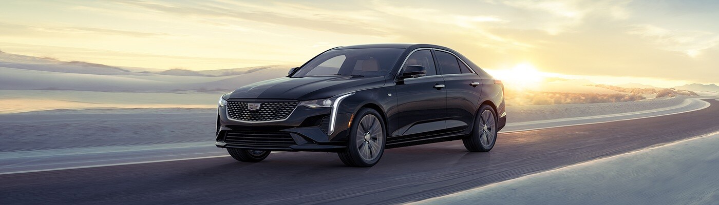 Dark CADILLAC CT4 sedan driving down a narrow snowy road with sun rising in the background new CADILLAC CT4