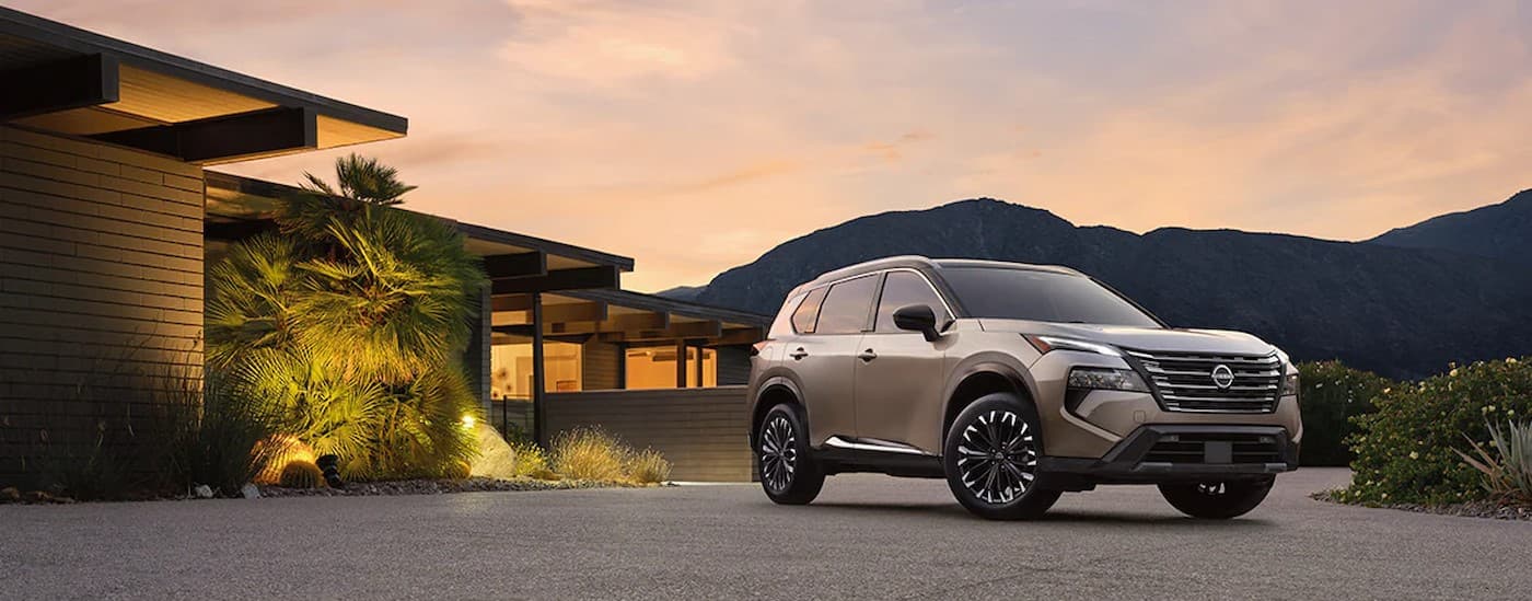 used%20car%20dealer%20near%20Grand%20Bay%20-%202024%20Nissan%20Rogue%20-%20House.jpg A tan 2024 Nissan Rogue parked near a house.