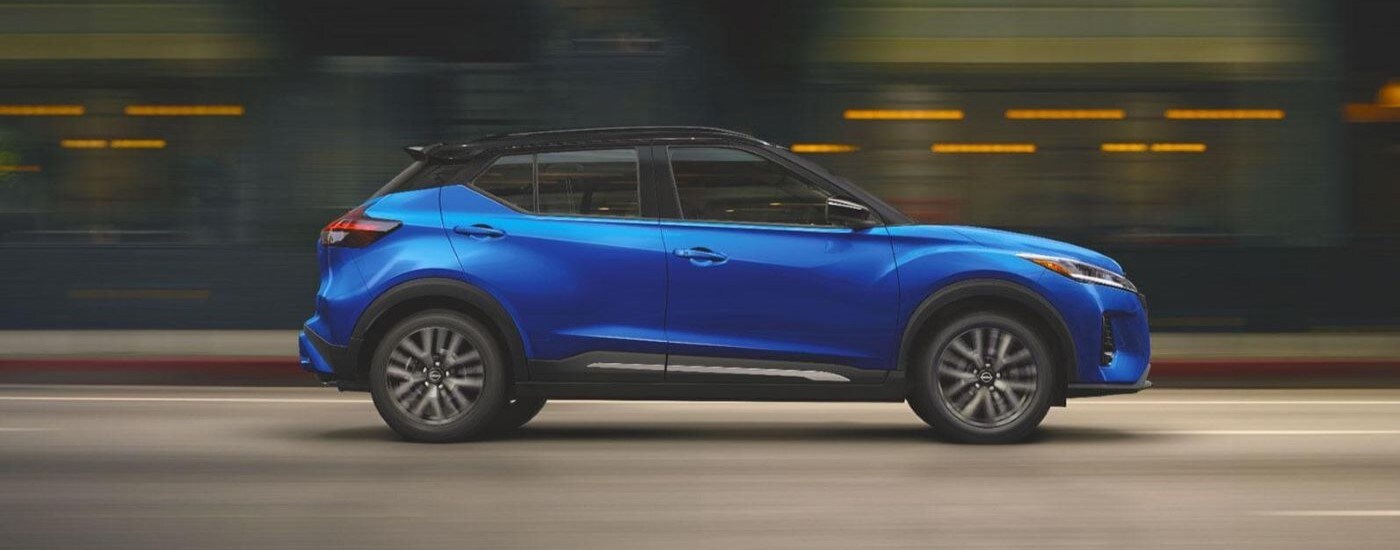 Side of a blue 2021 Nissan Kicks driving down a city street.