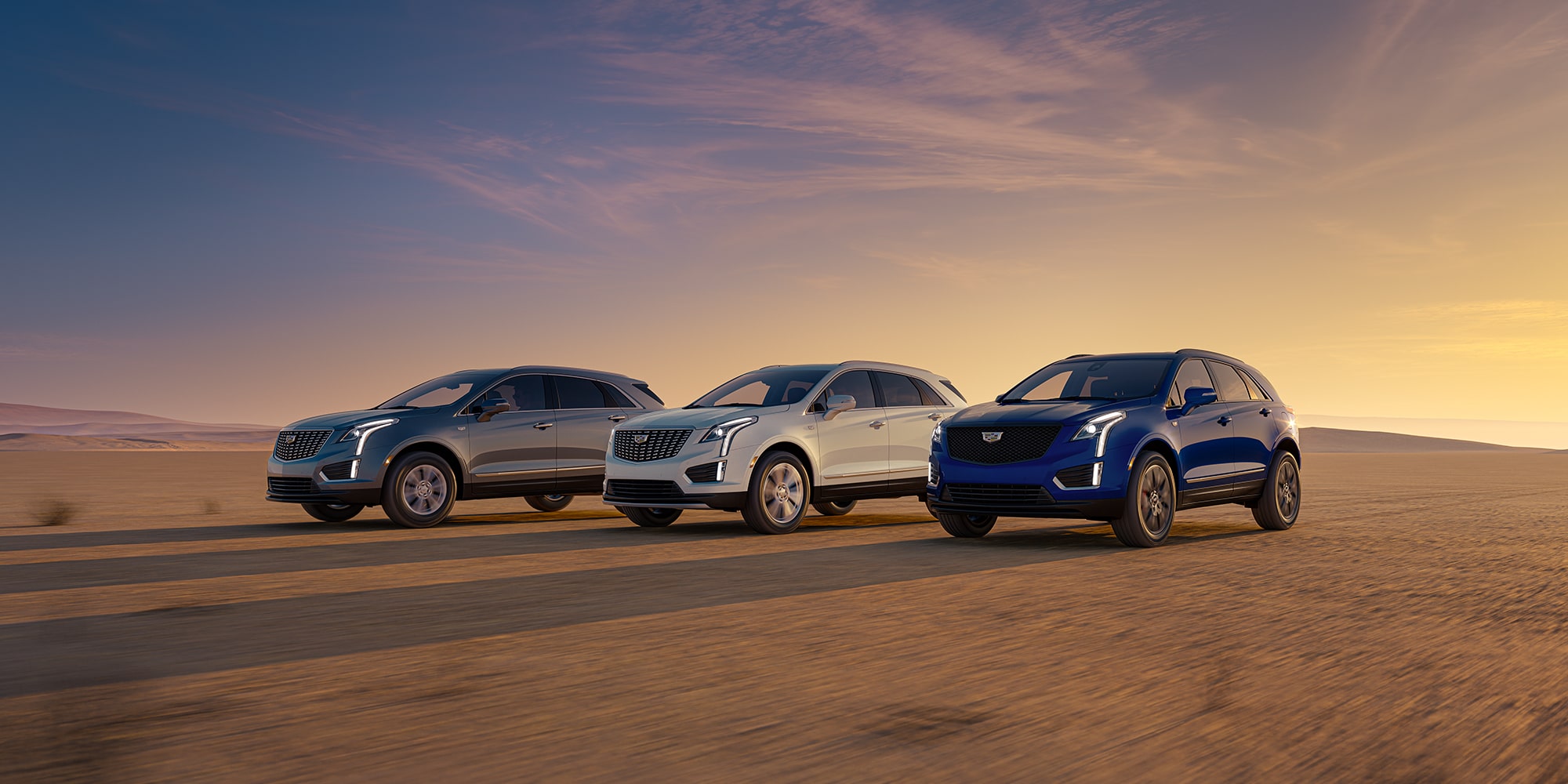 A trio of blue, white, and gray Cadillac XT5 models in the desert. A trio of blue, white, and gray Cadillac XT5 models in the desert.